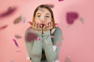 retrato de estúdio de uma jovem mulher feliz soprando confetes em forma de coração. conceito de dia dos namorados foto