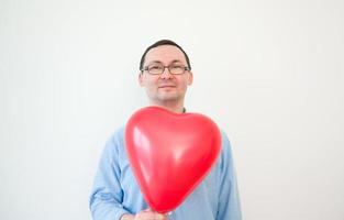 jovem de óculos segura balão de amor em fundo branco. dia dos namorados, aniversário, conceito de aniversário foto