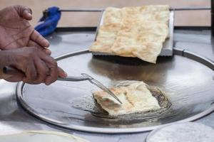 mão segurando uma espátula, fritando o roti em uma panela com óleo fervente. foto