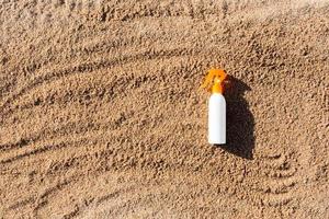 garrafa branca de loção bronzeadora na areia com espaço de cópia. protetor solar spf creme na praia do mar no conceito de férias de verão foto