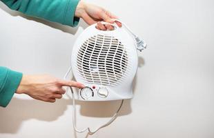 aquecedor isolado em um fundo branco. uma garota segura um aquecedor de ventilador de plástico e mostra o controlador de temperatura. foto