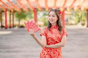 bela dama sorrindo alegremente segurando ang pao, envelopes vermelhos vestindo cheongsam parecendo confiante no templo budista chinês. comemore o ano novo lunar chinês, feriado da temporada festiva. foto