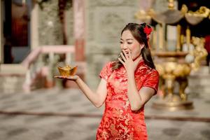feliz Ano Novo Chinês. mulher asiática usando vestido cheongsam qipao tradicional segurando dinheiro de ouro antigo no templo budista chinês. comemore o ano novo lunar chinês, feriado da época festiva foto