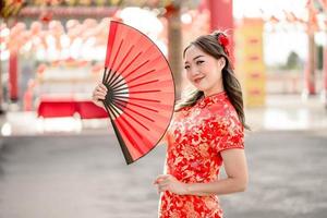 bela jovem asiática vestindo fantasia tradicional cheongsam qipao segurando ventilador no templo budista chinês. conceito de festival lunar do ano novo chinês foto