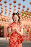 feliz Ano Novo Chinês. uma jovem usando vestido cheongsam qipao tradicional segurando dinheiro de ouro antigo e bolsa no templo budista chinês. comemore o ano novo lunar chinês, feriado da temporada festiva. foto