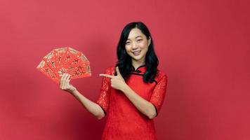 mulher feliz com cheongsam vermelho ou qipao mão apontando para abençoar cartão de fortuna isolado em fundo vermelho. texto chinês significa muita sorte grande lucro foto