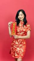 mulher bonita usando vestido cheongsam qipao tradicional segurando cartão de fortuna de bênção isolado em fundo vermelho. texto chinês significa muita sorte grande lucro foto