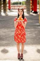 feliz Ano Novo Chinês. mulher asiática usando vestido cheongsam qipao tradicional segurando laranjas frescas reza para bênção de desejo e boa sorte no templo budista chinês. foto