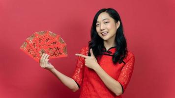 mulher bonita com cheongsam vermelho ou qipao mão apontando para abençoar o cartão da fortuna isolado em fundo vermelho. texto chinês significa muita sorte grande lucro foto