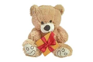 urso bebê peludo marrom com um presente em um fundo branco. brinquedo com uma caixa e uma fita vermelha. foto