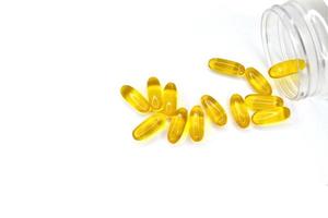 cápsulas douradas de pílulas derramadas de uma jarra em um fundo branco. medicamentos para tratamento. óleo de peixe, ômega-3 foto