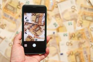 mão de homem tira uma foto de notas de euro no smartphone. Notas de 50 euros de papel monetário no fundo de uma tela de smartphone, o conceito de crescimento de negócios, investimento e renda.