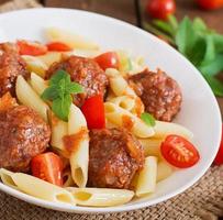 macarrão penne com almôndegas em molho de tomate em uma tigela branca foto