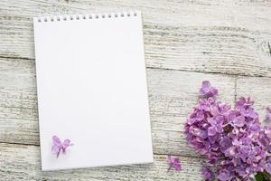 bloco de notas limpo com flores lilás de primavera em fundo branco de madeira foto