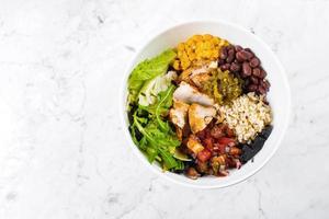 tigela de almoço mexicano em fundo de mármore. saladeira com milho, feijão vermelho, tomate com cebola roxa, jalapenios, peito de frango. vista superior, copie o espaço foto