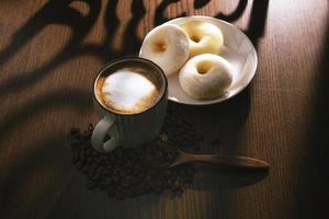 café com leite quente e rosquinhas na mesa de madeira atrás da janela foto