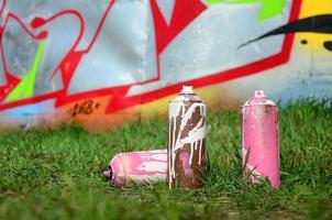 algumas latas de tinta usadas estão no chão perto da parede com uma bela pintura de grafite. arte de rua e conceito de vandalismo foto