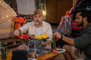 amigos de turistas de grupo acampando e fazendo um churrasco e bebendo cerveja-álcool com festa junto com diversão e felicidade no verão foto