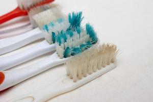 um monte de velhas escovas de dentes desgastadas com cerdas dobradas em um fundo branco foto