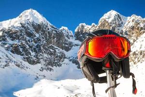 capacete de esqui e googles no bastão de esqui com picos nevados ao fundo foto