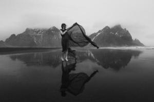 mulher de vestido com capa acenando na praia fotografia cênica monocromática foto