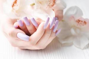 mãos de menina com manicure roxa delicada e flores de orquídea foto