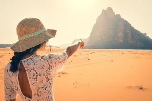 vista traseira posto de turismo feminino relógio apontar o dedo para os sete pilares do monumento da sabedoria na famosa reserva natural do deserto de wadi rum no oriente médio. visite a Jordânia explore o conceito foto