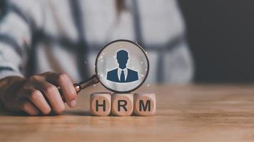 mão humana segurando uma lupa colocada em um bloco de madeira, hrm ou gerenciamento de recursos humanos, liderança em recrutamento, desenvolvimento de negócios, escolhendo a competência profissional dos funcionários dos líderes foto