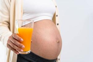 uma mulher grávida de 28 semanas segura um suco de laranja e escolhe uma dieta nutritiva para o desenvolvimento e crescimento saudável de seu filho ainda não nascido. foto