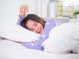 uma garota asiática está dormindo e sorrindo no travesseiro no quarto. sono feliz e bons sonhos foto