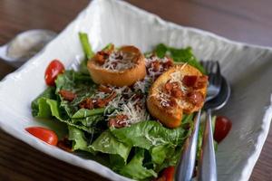 bacon de salada caesar e prato de pão em um prato branco colocado na mesa de jantar para café da manhã ou lanche. foto