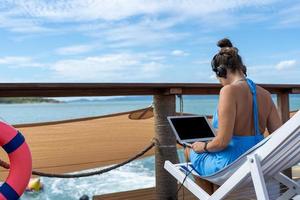 uma mulher sexy usa um laptop e fones de ouvido, funciona conectando-se à internet. uma mulher freelance trabalhando e descansando em um barco. vista para o mar com sol brilhante