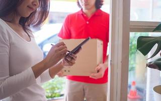 uma mulher está assinando em um smartphone para receber encomendas do remetente na porta da frente. encomende produtos online com entrega rápida. foto