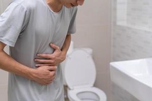 diarréia, dor abdominal, conceito de constipação. os homens têm contração e dor de estômago. homem segurando papel higiênico no banheiro. foto