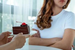 mãos entregando um prato de bolo de chocolate para uma jovem que está fazendo dieta, mas ela se recusa a comer. foto