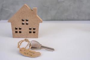 um modelo de uma pequena casa de madeira marrom e uma etiqueta de venda de casa anexada à chave da casa. conceito imobiliário, hipoteca, aluguel, comprar casa foto
