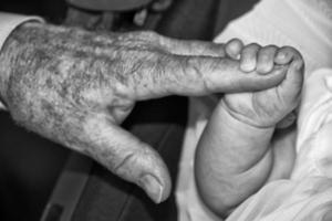 mãos de velho aposentado segurando um recém-nascido foto
