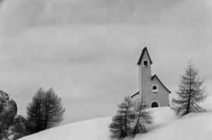 uma igreja pequena preto e branco da montanha no tempo de inverno do fundo da neve foto