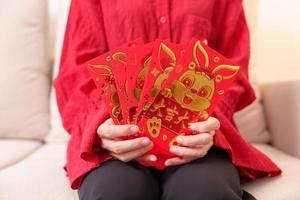 mulher segurando o envelope vermelho chinês com coelho dourado e palavra de bênção, presente de dinheiro para o feliz feriado do ano novo lunar. frase chinesa significa felicidade, saudável, sortudo e rico foto