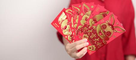 mulher segurando o envelope vermelho chinês com coelho dourado e palavra de bênção, presente de dinheiro para o feliz feriado do ano novo lunar. frase chinesa significa felicidade, saudável, sortudo e rico foto