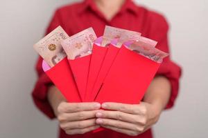 mulher segurando envelope vermelho chinês com presente de dinheiro baht tailandês para feliz feriado do ano novo lunar foto