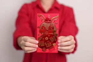 mulher segurando o envelope vermelho chinês com coelho dourado e palavra de bênção, presente de dinheiro para o feliz feriado do ano novo lunar. frase chinesa significa felicidade, saudável, sortudo e rico foto
