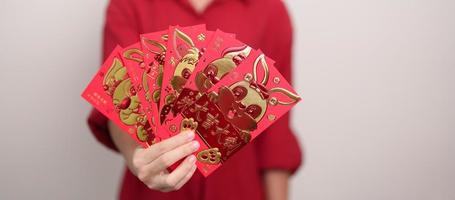 mulher segurando o envelope vermelho chinês com coelho dourado e palavra de bênção, presente de dinheiro para o feliz feriado do ano novo lunar. frase chinesa significa felicidade, saudável, sortudo e rico foto