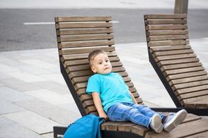 um menino de camiseta azul está descansando em uma chaise longue que fica no aterro. jornada. o rosto expressa emoções alegres naturais. fotos não encenadas da natureza