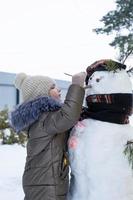 uma criança pinta o rosto de um boneco de neve com tintas - entretenimento de inverno e criatividade, esculpindo um boneco de neve no inverno ao ar livre. foto