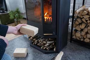 as mãos acendem a lareira com briquetes econômicos. briquetes de combustível feitos de serragem prensada para acender o forno - alternativa econômica de combustível ecológico para a lareira da casa. foto