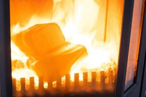 briquetes de combustível feitos de serragem prensada para acender o forno - alternativa econômica de combustível ecológico para a lareira da casa. a lenha está queimando no forno no interior foto