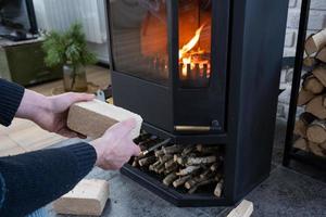 as mãos acendem a lareira com briquetes econômicos. briquetes de combustível feitos de serragem prensada para acender o forno - alternativa econômica de combustível ecológico para a lareira da casa. foto