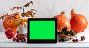abóboras, folhas de outono, cones e porta-retratos eletrônico com tela verde em pano de fundo claro. bandeira. foto