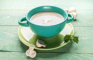 tigela de cerâmica turquesa com sopa de creme de cogumelos, cogumelos frescos e salsa na placa verde sobre fundo verde de madeira. foto